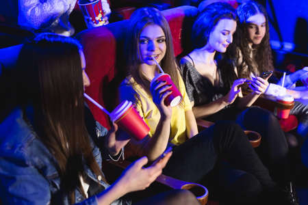 Young beautiful women drink from a glass in the cinema and watch a movieの写真素材