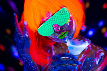 Fashion model woman drinking alcoholic cocktail in neon light, disco night club. Beautiful dancer...