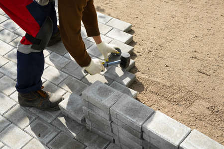 Hands of a worker installing concrete blocks, paving slabs with a rubber hammer