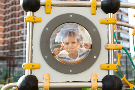 Boy is playing and making faces on a modern playground in the courtyard of a new residential complexの写真素材