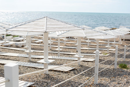 White wooden beach umbrellas, paths and deck chairs on the seashore, ocean.の写真素材