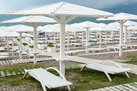 White wooden beach umbrellas, paths and deck chairs on the seashore, ocean.の写真素材
