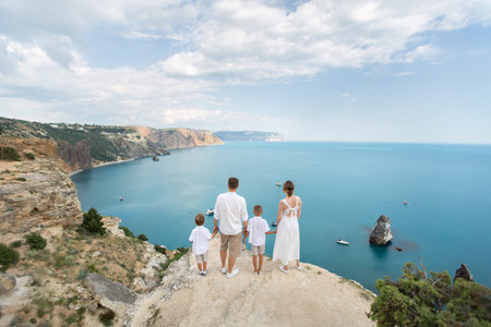 Happy family of four is standing on a cliff. View from the back.の写真素材