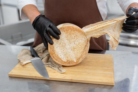 Cheese maker removes the wrapper from the cheese after ripening in the kitchen of the cheese factoryの写真素材