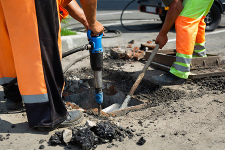 A road worker is dismantling street asphalt and old drainage with a jackhammer.の写真素材