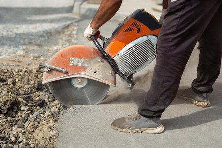 A road builder in uniform cuts off the old asphalt with a hand grinder according to the markings.の写真素材