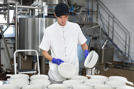 A worker in medical gloves shows the process of producing cottage cheese at a dairy factory.の写真素材