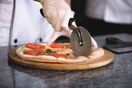 The cook cuts pizza with a round knife.の写真素材
