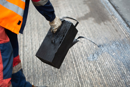 A worker pours liquid asphalt, molten bitumen from a bucket of resin.