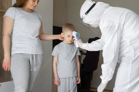 Doctor checks boys body temperature using infrared forehead thermometer gun for virus covid-19の写真素材
