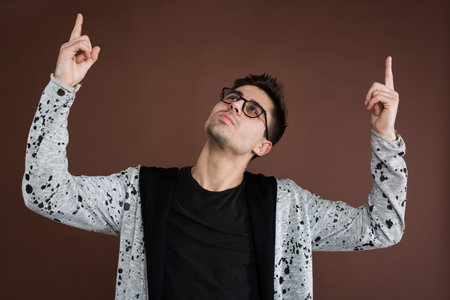 Happy cheerful young guy gesturing up with fingers.の写真素材