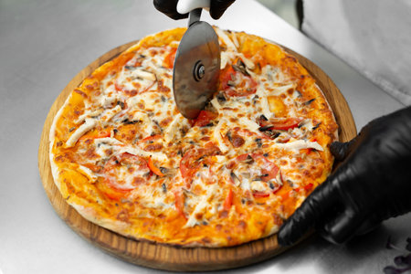 Closeup hand of chef cuts freshly prepared pizza slices at kitchen.の写真素材