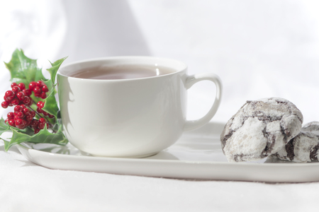 Yummy chocolate crinkle biscuits with a cup of coffee on a white background, next to the white cup there is a xmas red flower, close upの写真素材