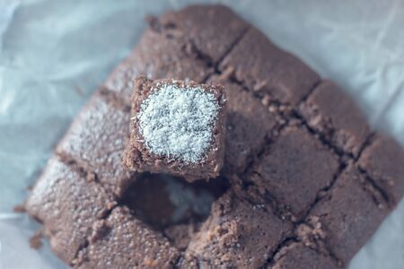 Homemade brownie with desiccated coconut on a white baking paper, close up, above vantage point,...