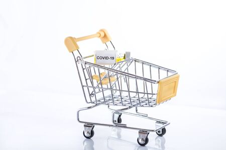 Yellow shopping cart with Covid-19 vaccine on a white background, isolated, close up. Be careful with coronavirus while shopping!の写真素材