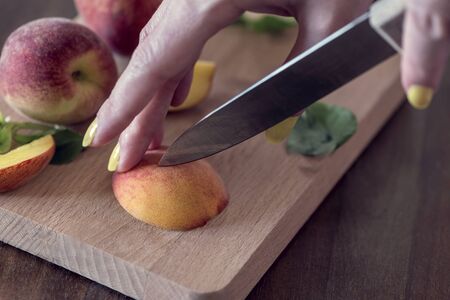 A woman cutting fresh peaches on a wooden cutting board, close up, still life photography