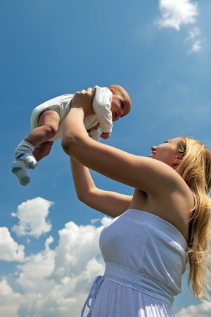 Happy young mother lifting her baby boy high upの写真素材