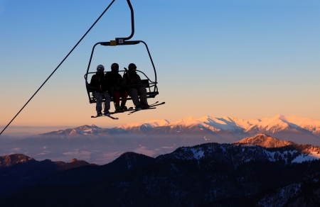Chair ski lift with skiers over blue sky and mountains の写真素材