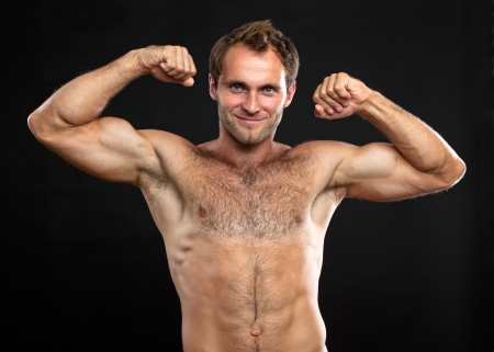 Waist-up portrait of muscular man flexing his biceps against black backgroundの写真素材