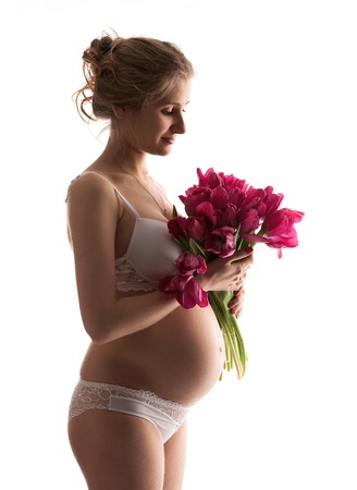 Beautiful young pregnant woman in lingerie holding flowersの写真素材