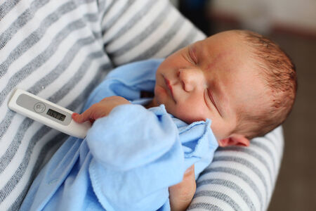 Father taking newborn son s temperature with thermometer