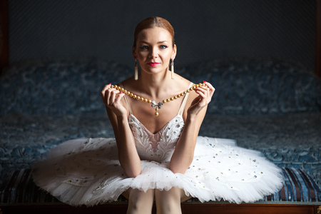 Ballerina sitting on bed holding pearl necklaceの写真素材
