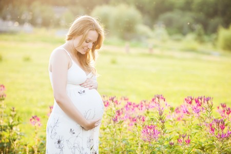 Young pregnant woman looking at her belly and smiling in a park