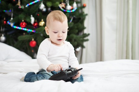 Toddler boy holding RC controller while sitting on bed at home at christmas timeの写真素材