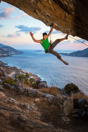 Cheerful rock climber waving his hand while climbing at sunsetの写真素材