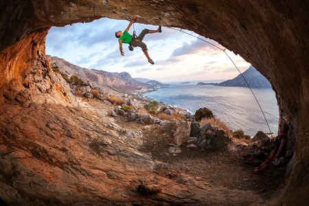 Male rock climber climbing along a roof in a cave at sunset. Kalymnos Island, Greeceの写真素材