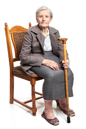Senior woman with walking stick sitting on chair over white backgroundの写真素材