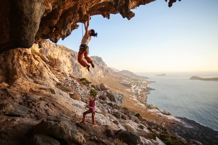 Young woman lead climbing on overhanging cliff, female partner belayingの写真素材