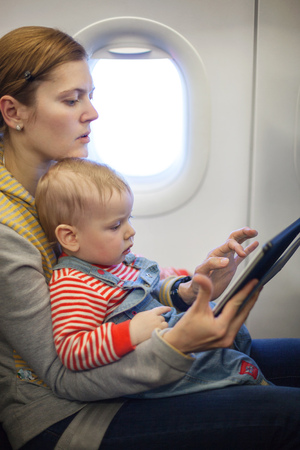 Caucasian mother and toddler son using tablet pc during while on board of airplaneの写真素材