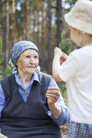 Great grandmother and toddler boy talking during walk in park or forestの写真素材