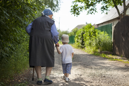Great grandmother and toddler boy holding hands while walking down street in countrysideの写真素材
