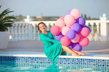 Happy young woman with a bunch of balloons after jumping into a swimming pool in a dressの写真素材
