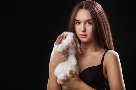 Beautiful young woman with a pet rabbit against black backgroundの写真素材
