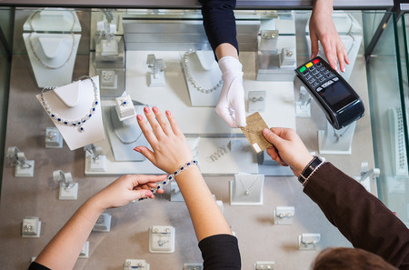 Young woman buying a golden necklace with blue gemstones and paying with a credit cardの写真素材