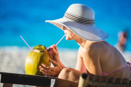 Young woman drinking coconut juice while relaxing on the beachの写真素材