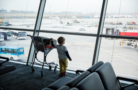 Little boy standing at window in airport and looking at landing fieldの写真素材
