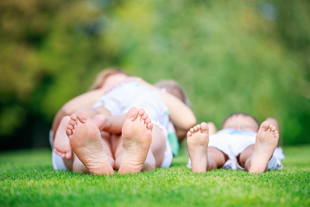 Young woman breastfeeding toddler son, eldest son relaxing on grass beside mother, shallow depth of fieldの写真素材