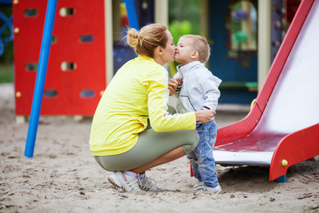 Mother kissing son after catching him at bottom of playground slideの写真素材
