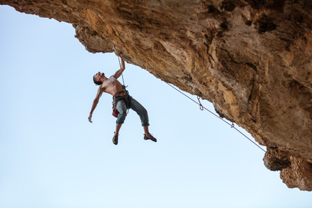 Male rock climber hanging with one hand on on a cliffの写真素材