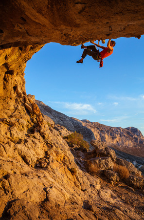Male climber on overhanging rock against beautiful view of coast belowの写真素材