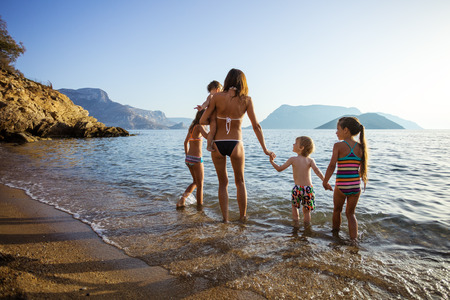 Young woman with four children walking in shallow sea watersの写真素材