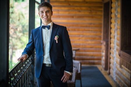 Handsome young bridegroom standing by window and smilingの写真素材