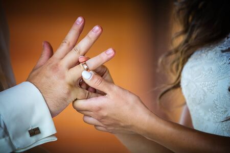 Bride putting ring on groom's finger, cropped view indoorsの写真素材