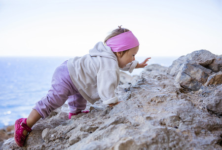 Happy little girl climbing on rock on beachの写真素材