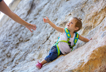 Little girl in climbing gear stretching out hand to motherの写真素材