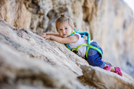 Little girl in safety harness climbing up cliffの写真素材